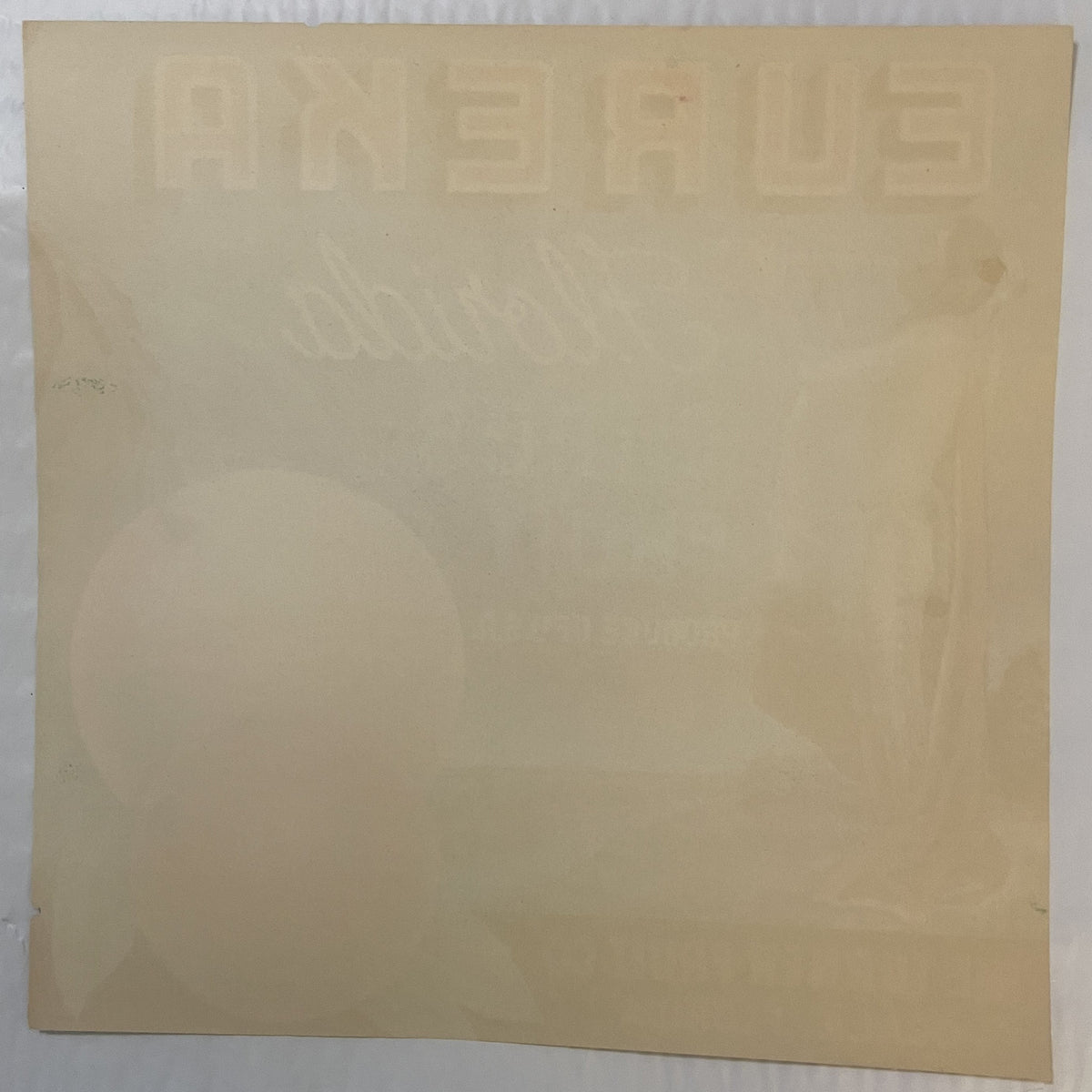 Cream-colored vintage citrus crate label with embossed text and faint Native American imagery, photographed flat against whit