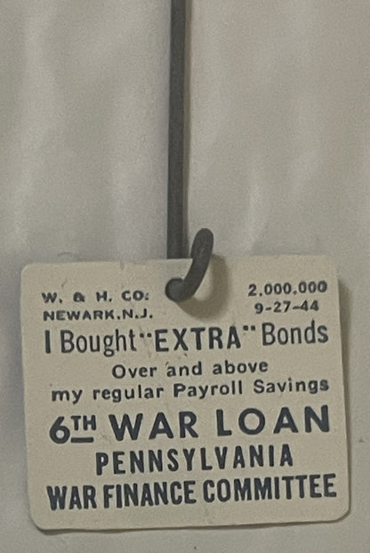 Cream-colored WWII war bond badge from Newark, N.J., dated 9-27-44, hanging from black metal clasp against gray curtain backd