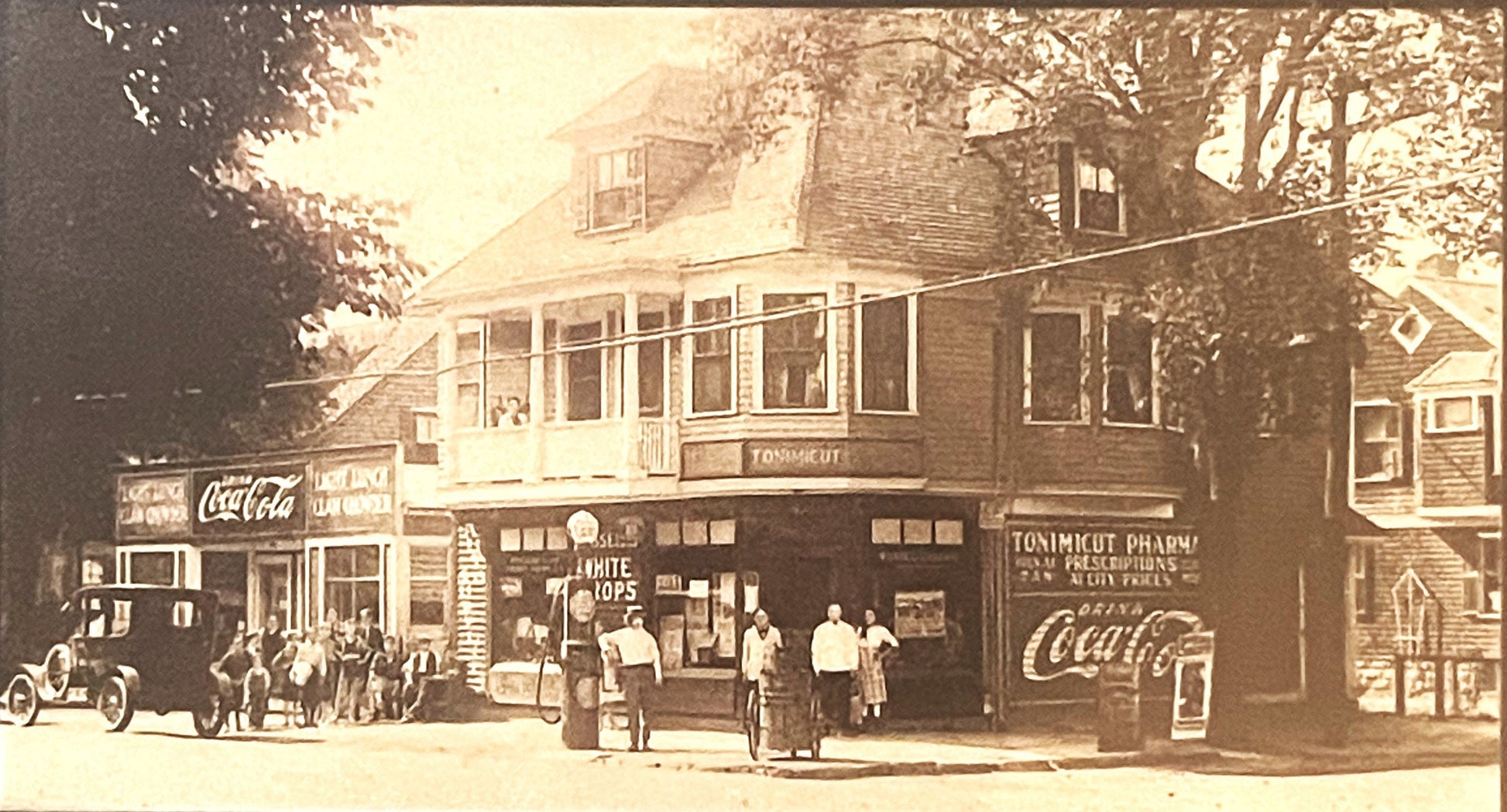 Sepia-toned vintage street scene showing storefront with "White Tops" and "Tonimicut Pharmacy" signs, Coca-Cola advertising, 
