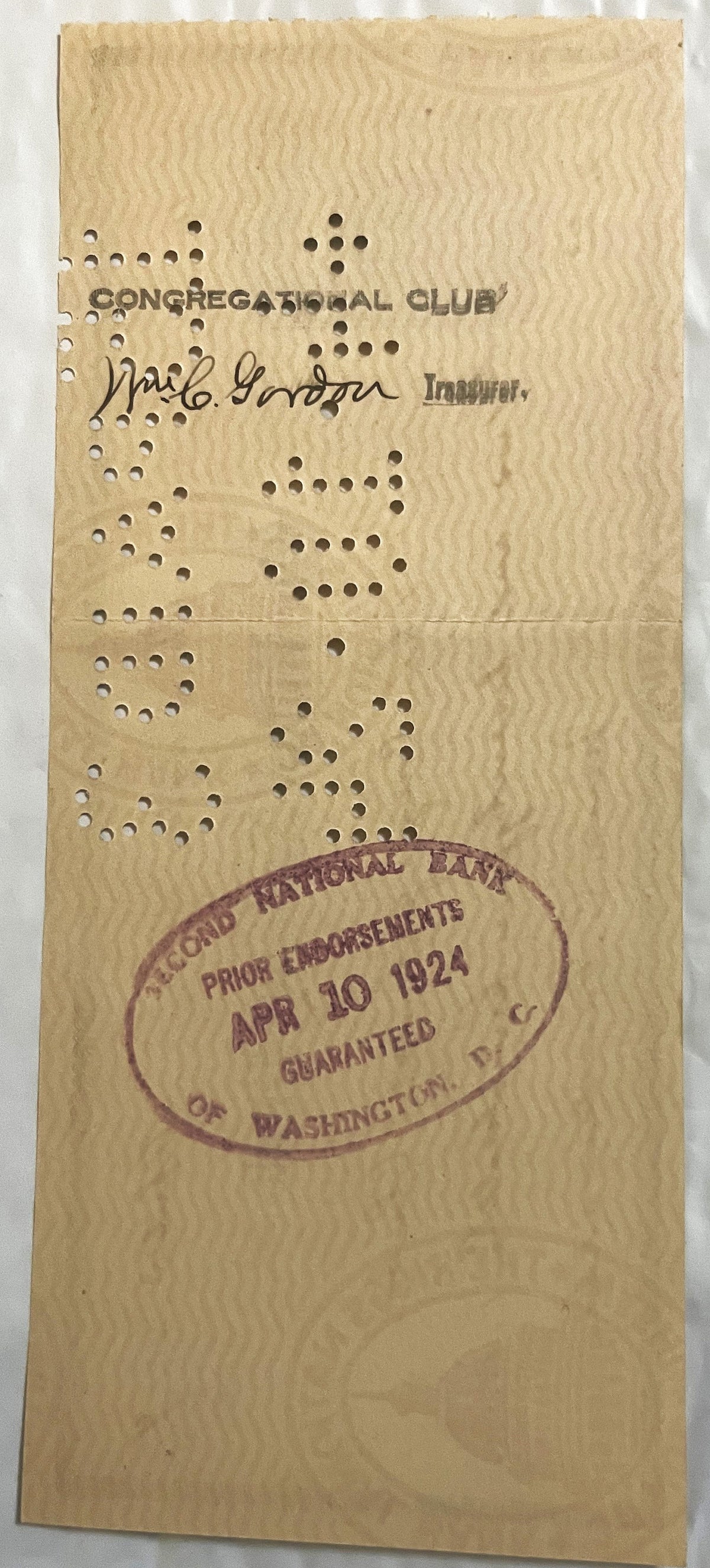 Back of a later Riggs National Bank check on wavy safety-tint paper with a hand-signed endorsement, an oval bank clearing stamp and punch-cancellation holes