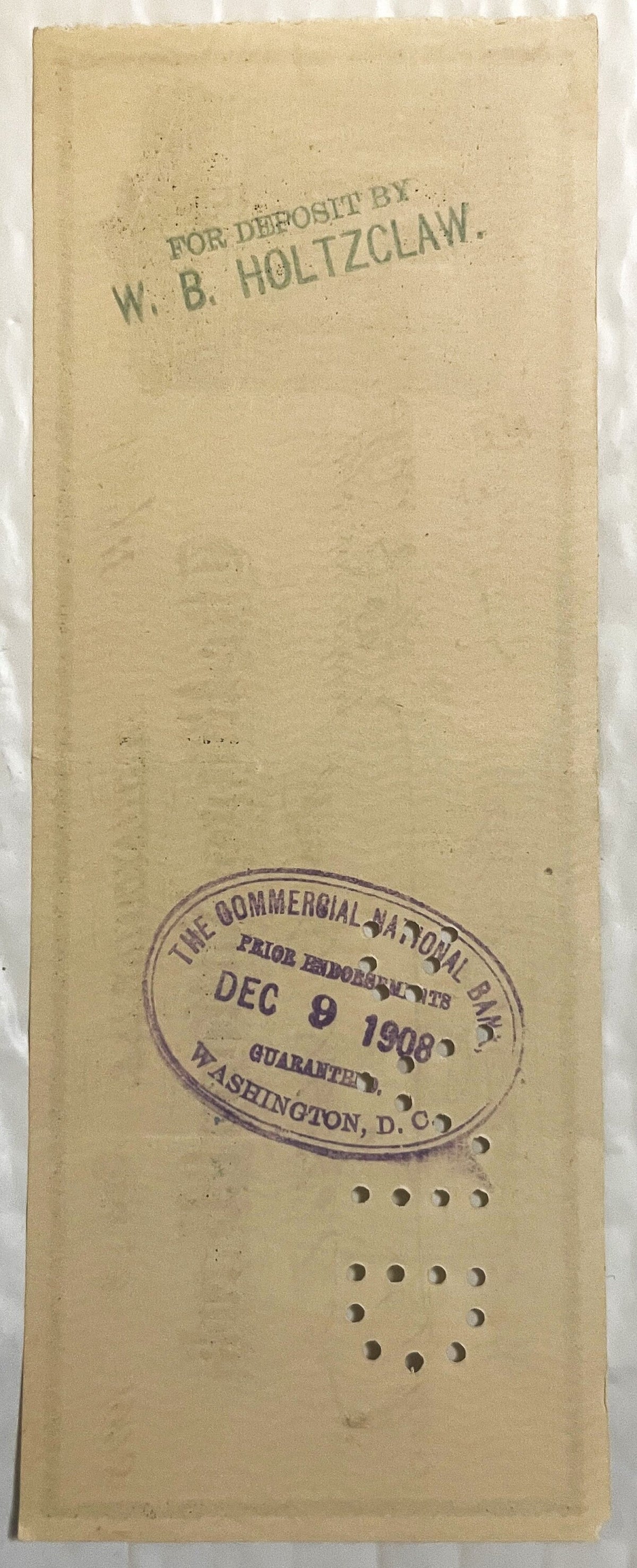 Back of an antique Riggs National Bank check with a rubber-stamped deposit endorsement, an oval bank clearing stamp and punch-cancellation holes