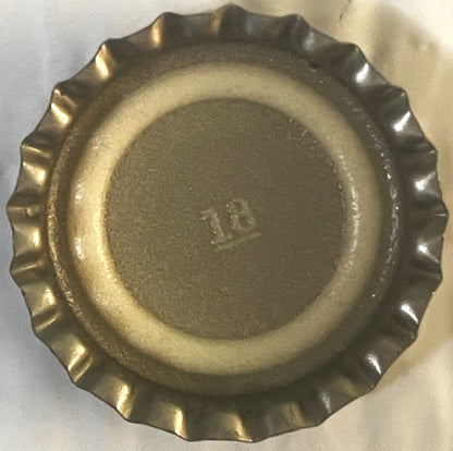 Vintage metal bottle cap with corrugated ridged edges, viewed from above on light background, showing embossed text in center