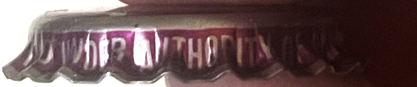 Close-up of a ridged metal bottle cap with purple and white striped design and embossed text, shown at an angle against a dar