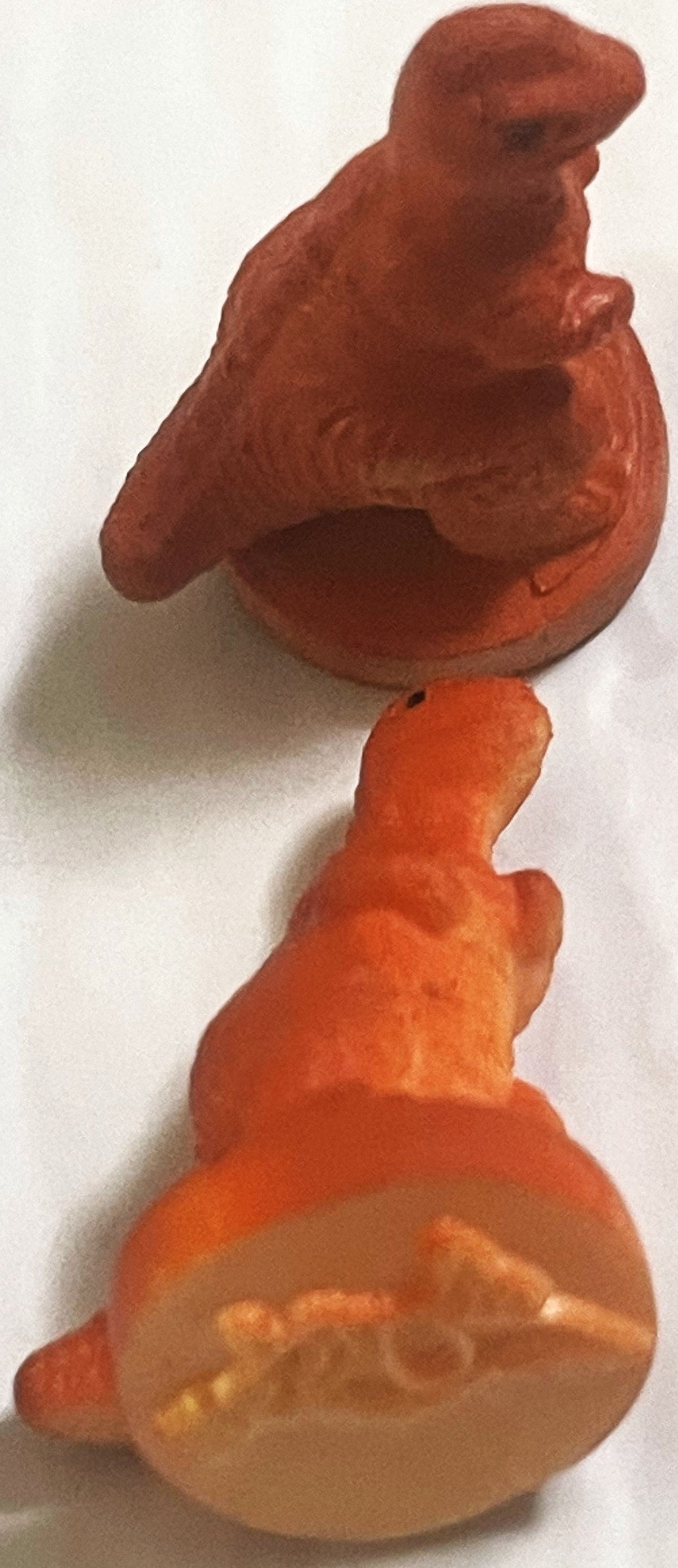 Two orange and rust-colored rubber T-rex dinosaur stamps on white, the lower one turned to show the raised dinosaur outline on its round base
