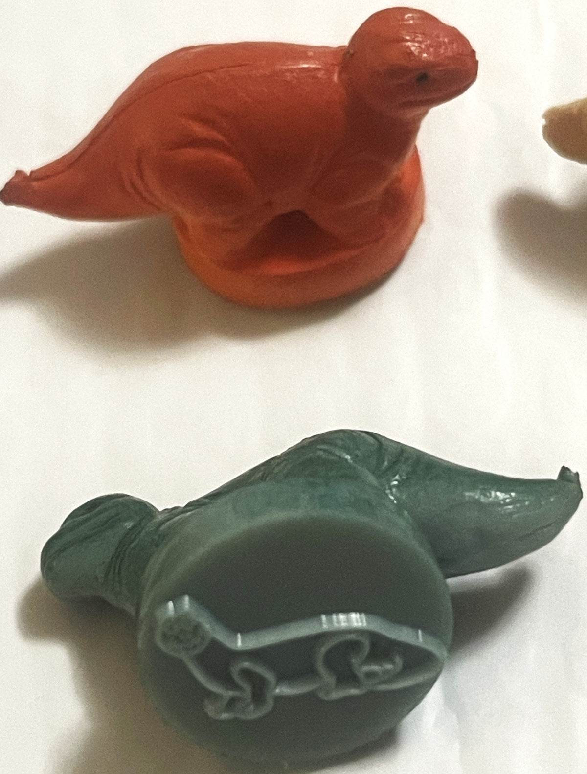 Two vintage rubber dinosaur stamps on white: a red dinosaur above, and a green long-necked dinosaur turned to show the long-necked dinosaur outline on its stamp base