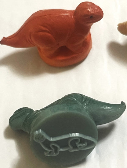Two vintage rubber dinosaur stamps on white: a red dinosaur above, and a green long-necked dinosaur turned to show the long-necked dinosaur outline on its stamp base
