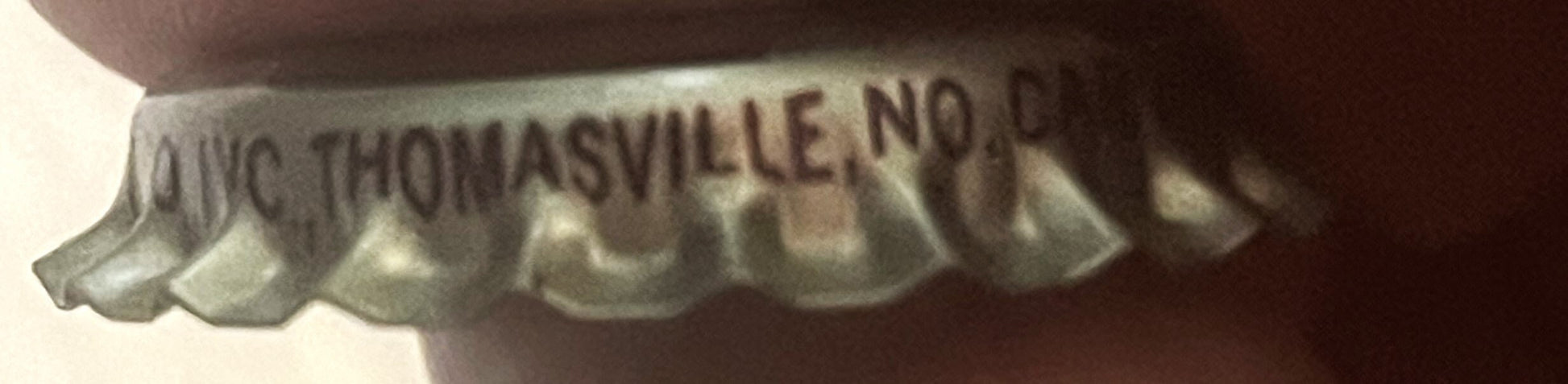 Close-up of vintage bottle cap showing embossed text "Big B Thomasville, NC" with corrugated metal ridges, held at an angle