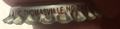 Close-up of vintage bottle cap showing embossed text "Big B Thomasville, NC" with corrugated metal ridges, held at an angle