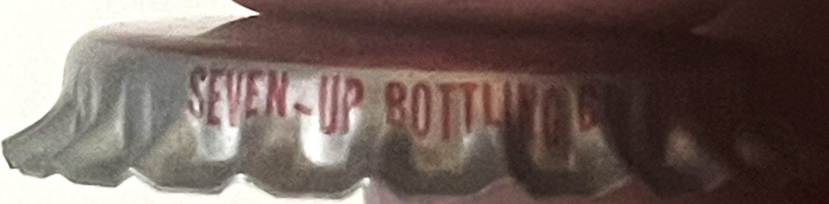 Corrugated bottle cap with embossed text "SEVEN-UP BOTTLING" visible, shown in close-up detail against dark background