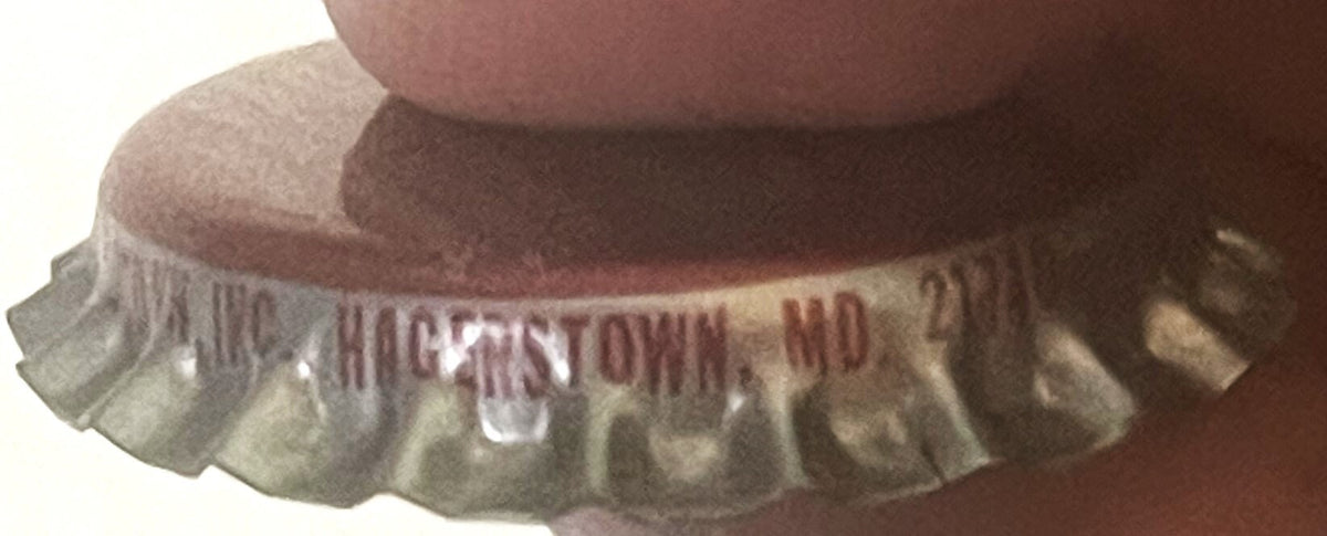 Vintage bottle cap held in hand showing ridged metal edges and partial text reading "GHOSTTOWN" and "MD