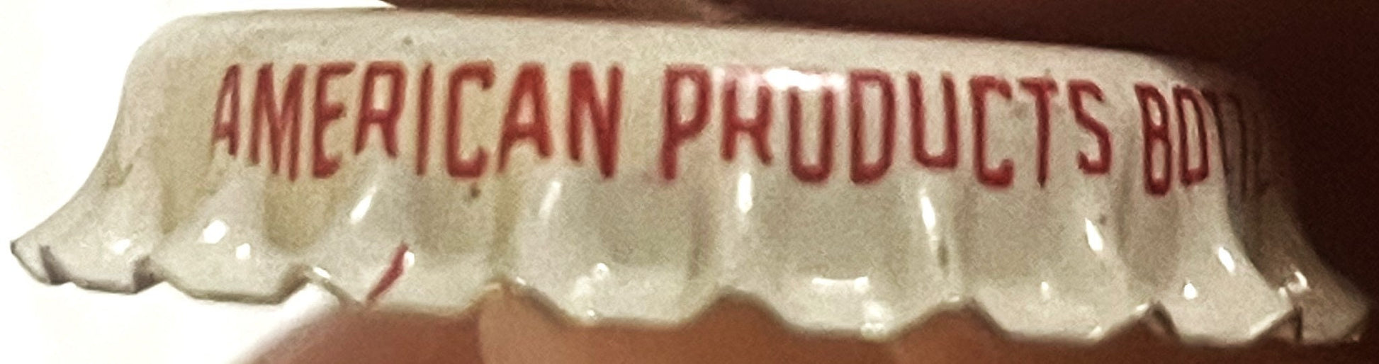 Vintage bottle cap with scalloped white edges and red "AMERICAN PRODUCTS BOD" text, shown close-up at an angle