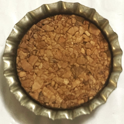 Overhead view of a vintage root beer bottle cap with ridged metal edges and tan cork or paper liner showing age spots and wea