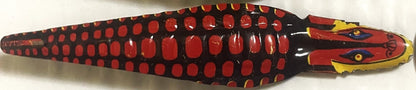 Red and black tin snake toy with yellow head, gold eyes, and mouth mechanism, viewed from above against white background