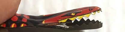 Vintage red and black snake tin clicker toy with open mouth showing yellow teeth, held in a hand for scale.
