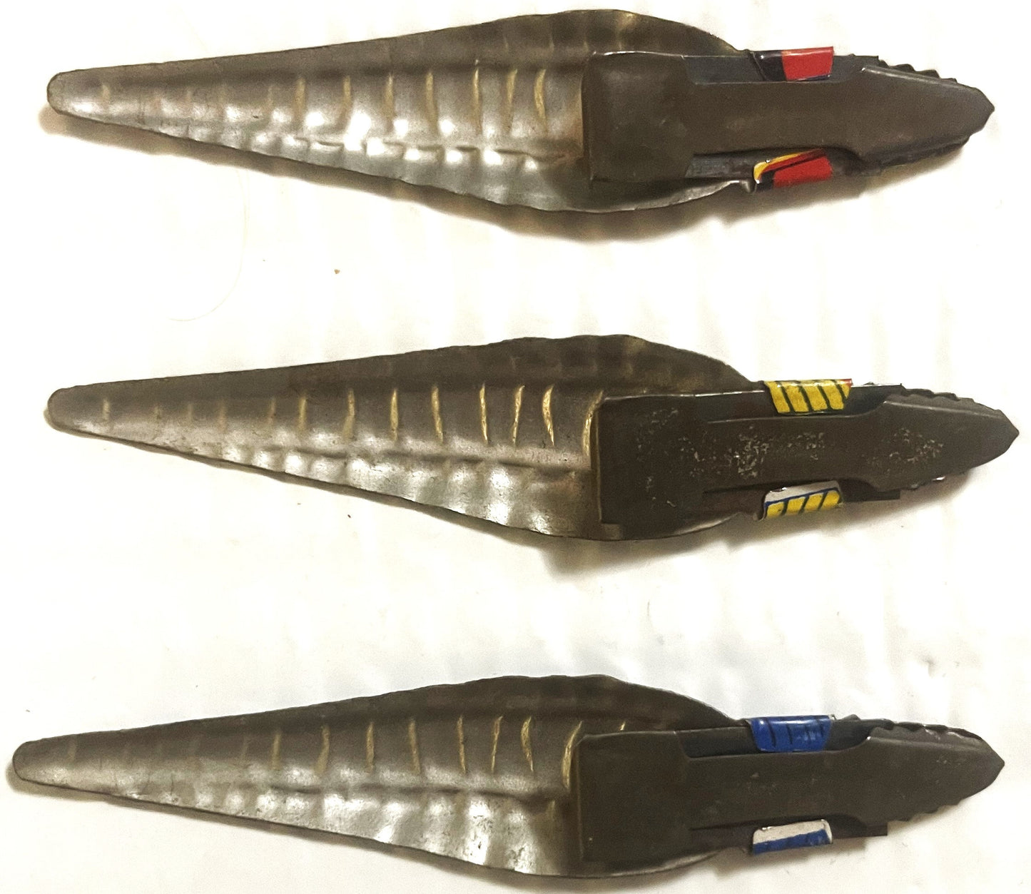 Three vintage tin snake clicker toys with silver bodies and black heads, each with different colored stripe details on the ta