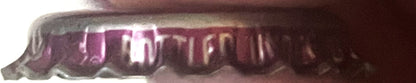 Close-up of burgundy and cream vintage bottle cap with embossed text, shown at angle against white background
