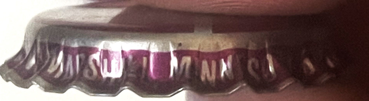 Vintage bottle cap close-up showing burgundy and cream ridged crown with partial text visible, photographed at an angle again