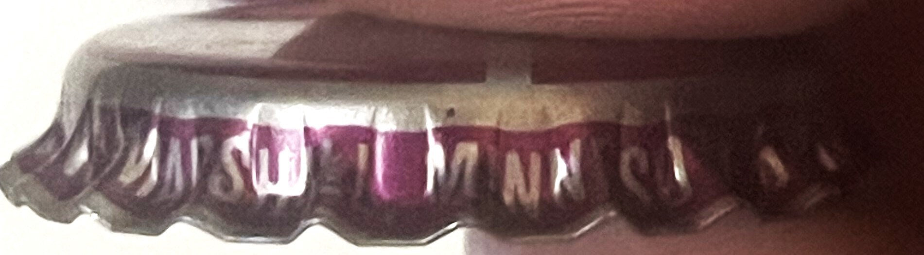 Vintage bottle cap close-up showing burgundy and cream ridged crown with partial text visible, photographed at an angle again