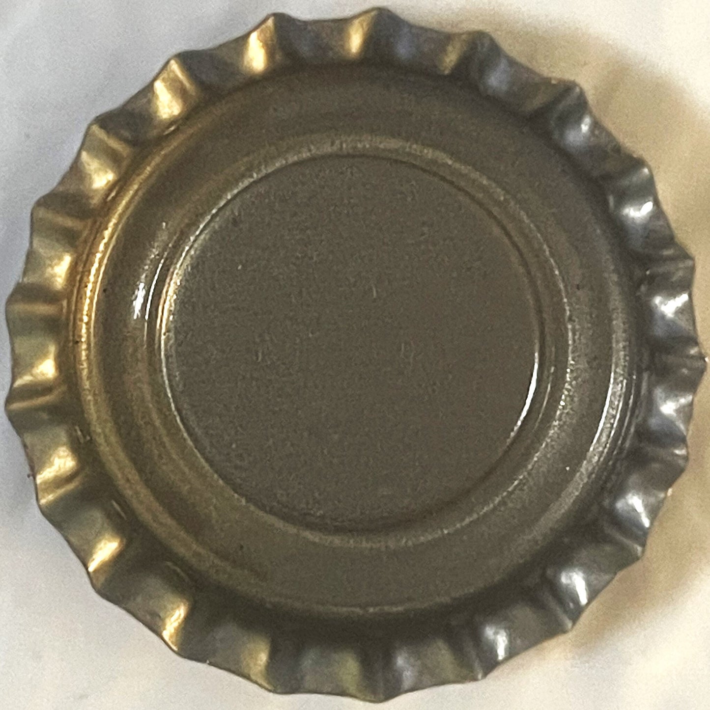 Corrugated metal bottle cap with ridged crown edge, shown flat from above on white surface, displaying worn gold and silver f