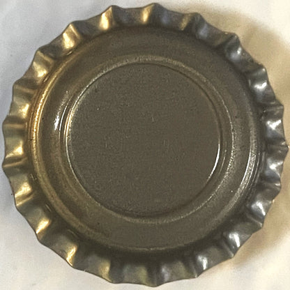 Corrugated metal bottle cap with ridged crown edge, shown flat from above on white surface, displaying worn gold and silver f