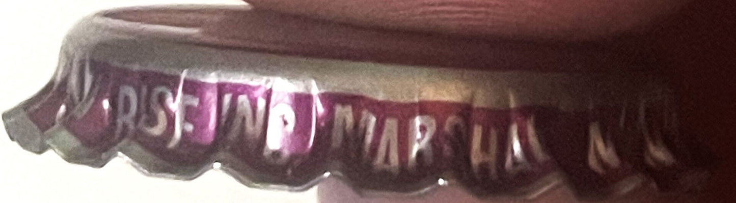 Vintage purple and white ridged bottle cap with embossed text, shown at an angle against a dark fabric background