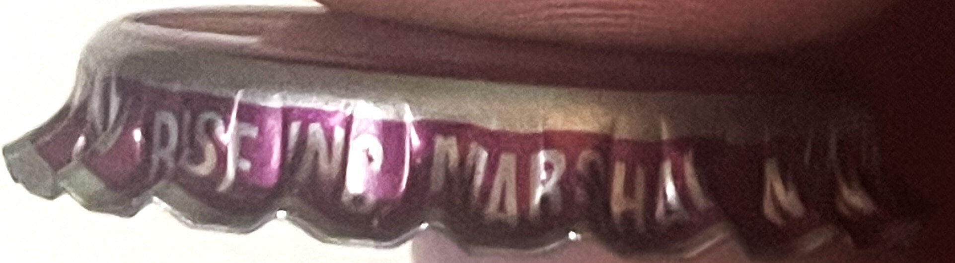 Vintage purple and white ridged bottle cap with embossed text, shown at an angle against a dark fabric background