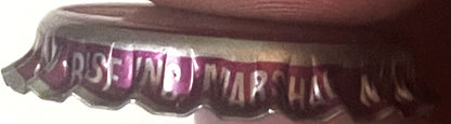 Vintage purple and white ridged bottle cap with embossed text, shown at an angle against a dark fabric background
