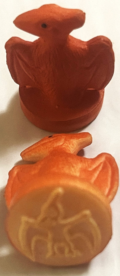 Two vintage rubber dinosaur stamps in rust and orange tones photographed against white background, showing embossed detail