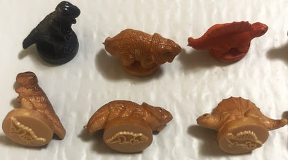 Six vintage rubber dinosaur stamps in brown and black on white surface, showing embossed details on flat