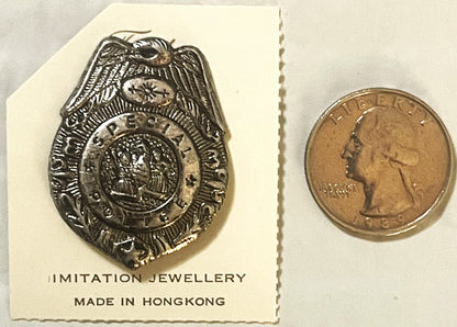 Silver police badge pin with eagle and shield design next to US quarter for scale, mounted on card labeled "Imitation Jewelle
