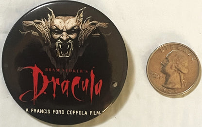 Vintage Dracula pin button with demon face artwork and red text, shown next to quarter for scale on white background