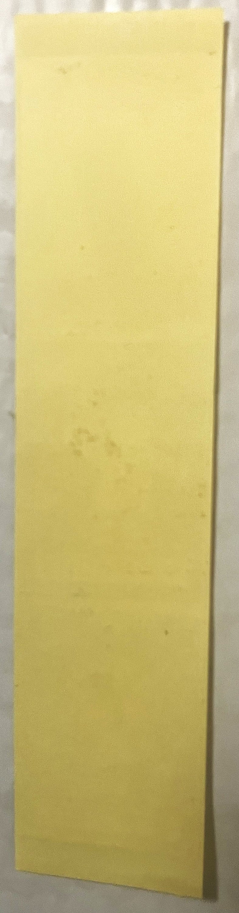 Blank yellow rectangular sheet or panel leaning against white wall, shown at an angle for scale