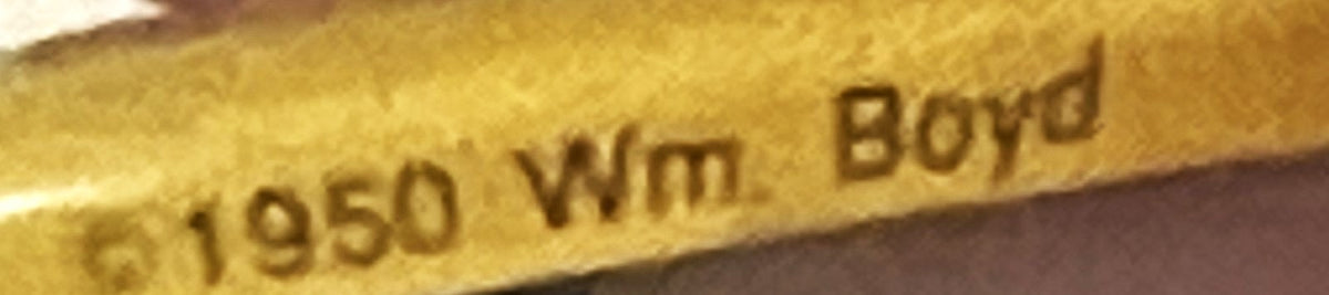 Close-up of embossed gold metal pin showing "1950 Wm Boyd" text against brown background