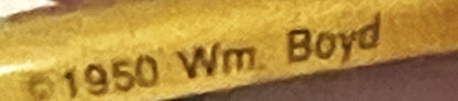 Close-up of embossed gold metal pin showing "1950 Wm Boyd" text against brown background