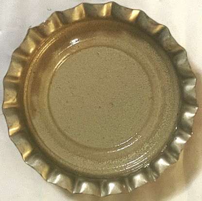 Gold metallic bottle cap with crimped edges shown flat against white background, surface shows wear and patina