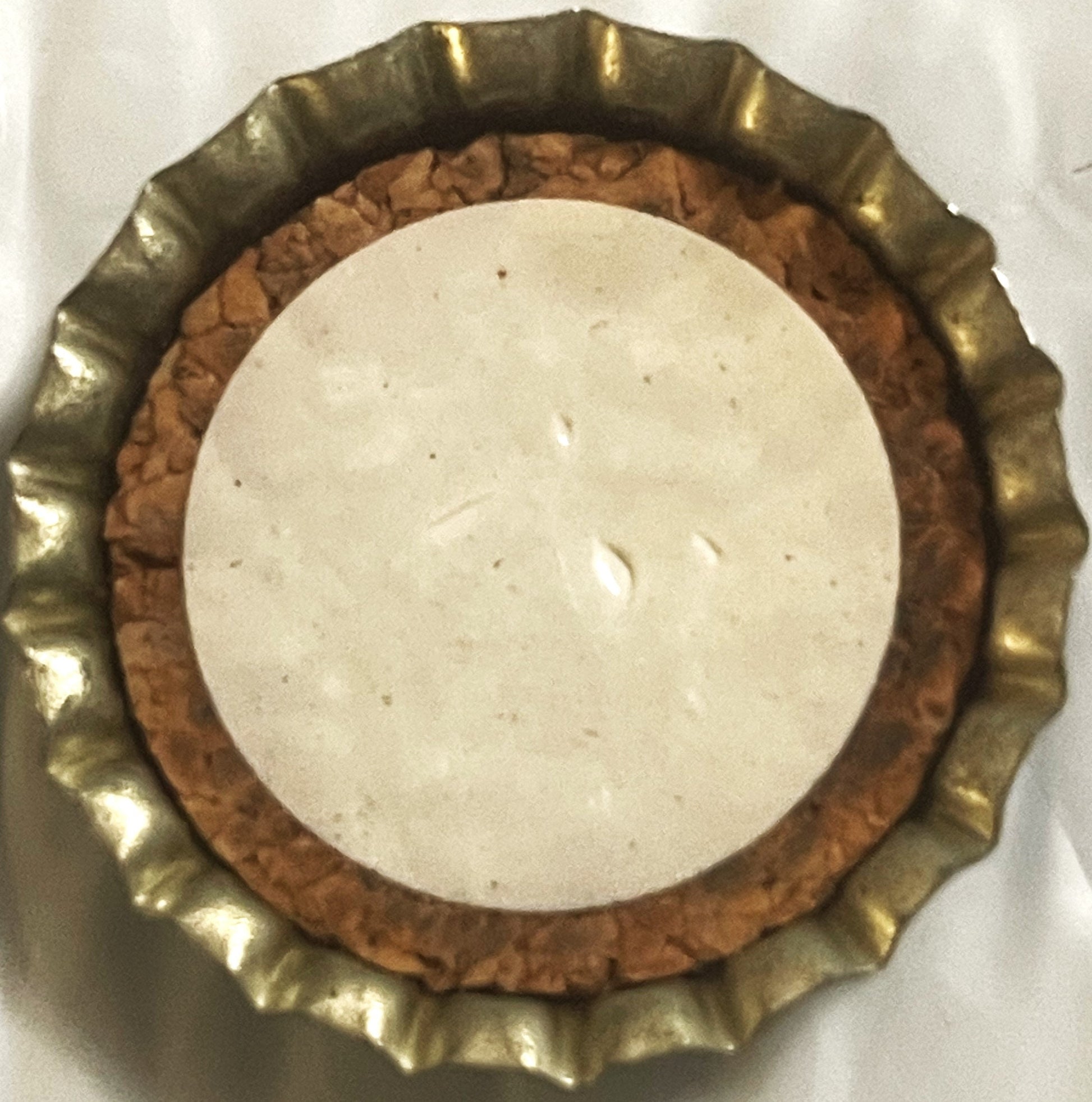 Overhead view of a cork bottle cap with brass-colored ridged rim and tan cork center on white background.