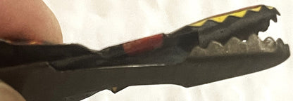 Black tin snake toy with yellow stripe detail held in hand, mouth mechanism visible showing articulated jaw design