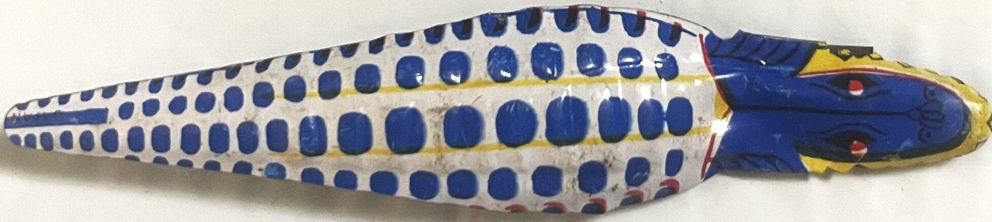 Vintage tin fish clicker toy with blue and white spotted body, yellow and blue head, shown from above against white backgroun