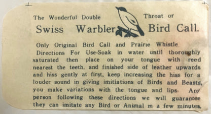 Cream-colored vintage instruction card for Swiss Warbler bird call with printed text and small leaf illustration, close-up of