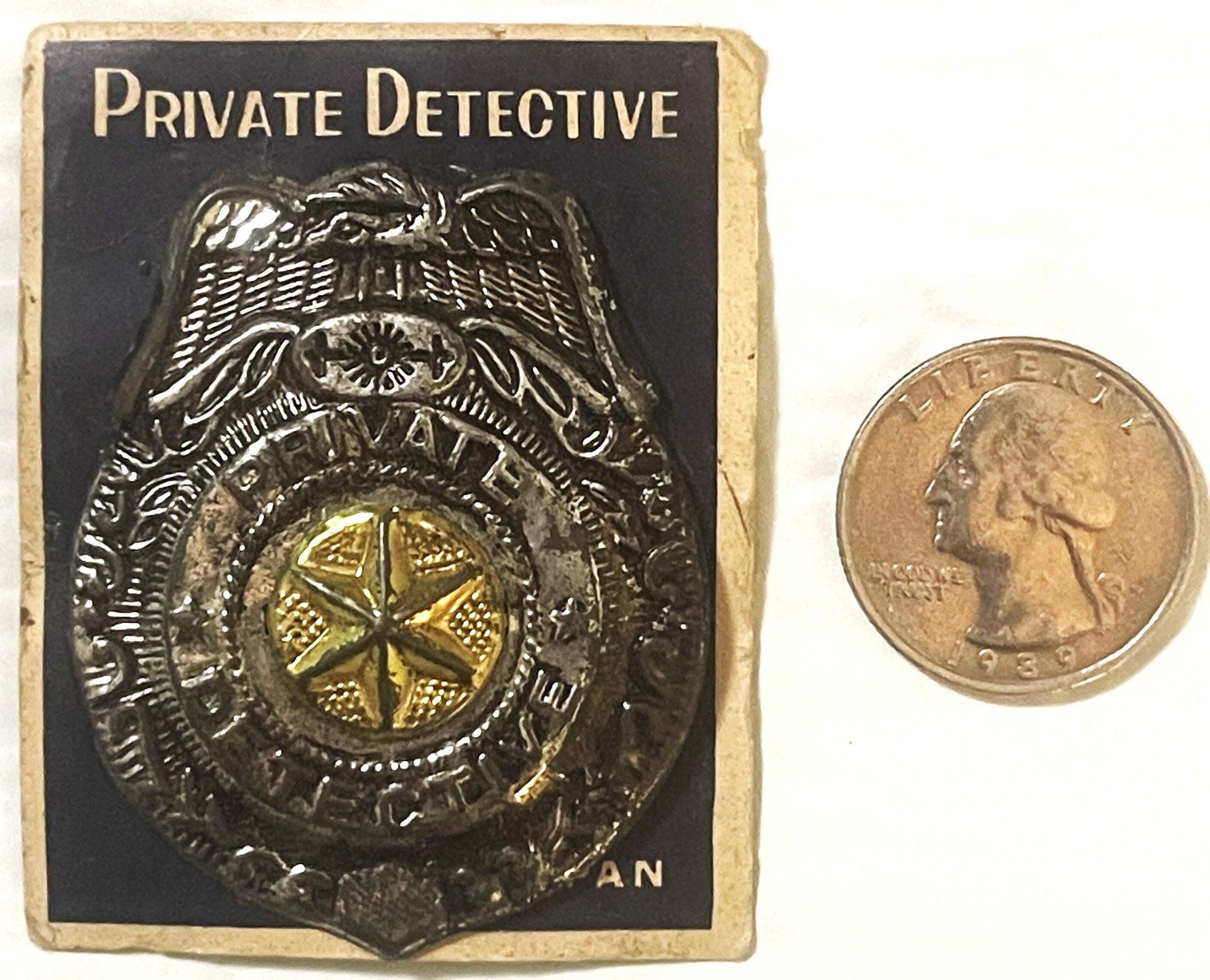 Vintage tin private detective badge on original card with eagle and gold star, shown next to quarter for scale