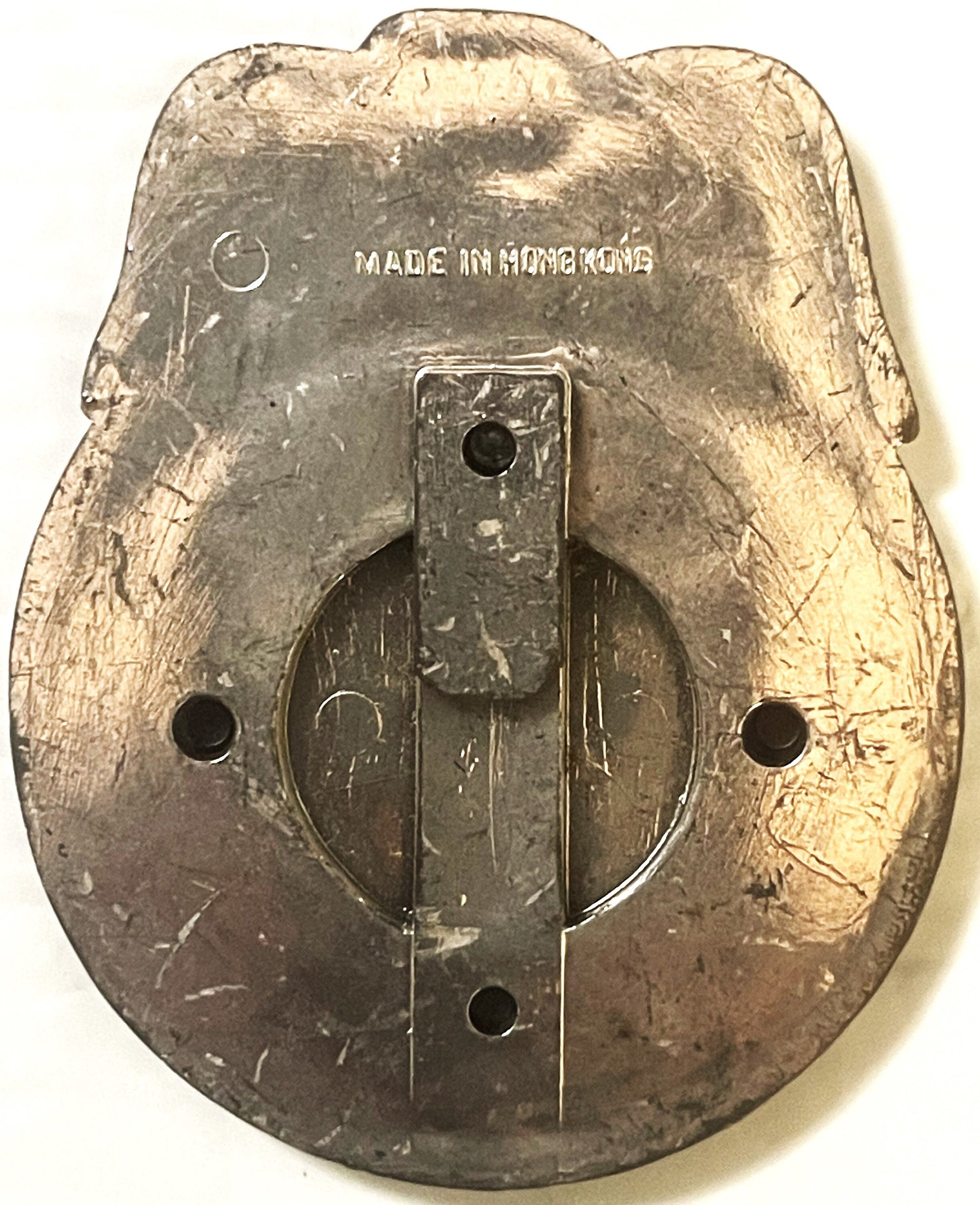 Back of vintage tin badge with "MADE IN HONG KONG" text, showing mounting holes and worn metallic surface