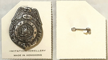 Vintage police badge pin with eagle and profile portrait on cream card labeled "Imitation Jewellery Made in Hong Kong," shown