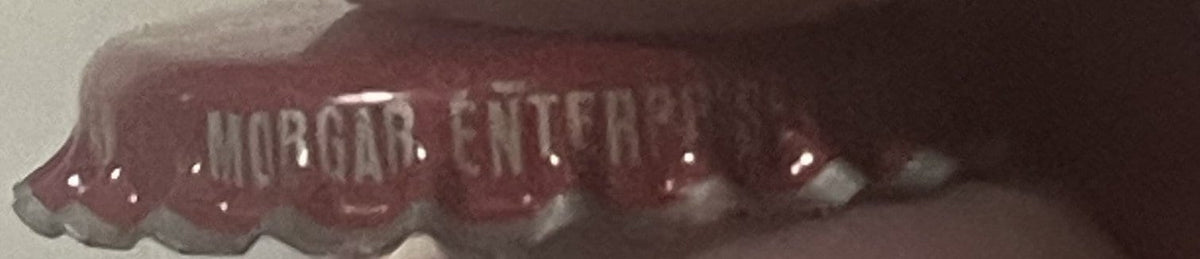Close-up of a crimped metal bottle cap with "WHISTLE" text visible on a deep red background against a light surface