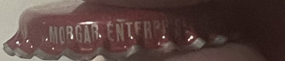 Close-up of a crimped metal bottle cap with "WHISTLE" text visible on a deep red background against a light surface