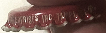 Close-up of a crimped bottle cap with maroon and gray coloring, showing embossed text "ENTERPRISES INC" visible on the ridged