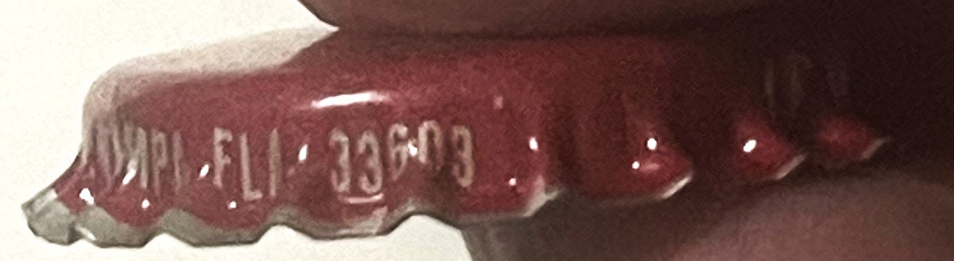 Close-up of maroon bottle cap with embossed text, held in hand showing ridged edge detail and partial lettering