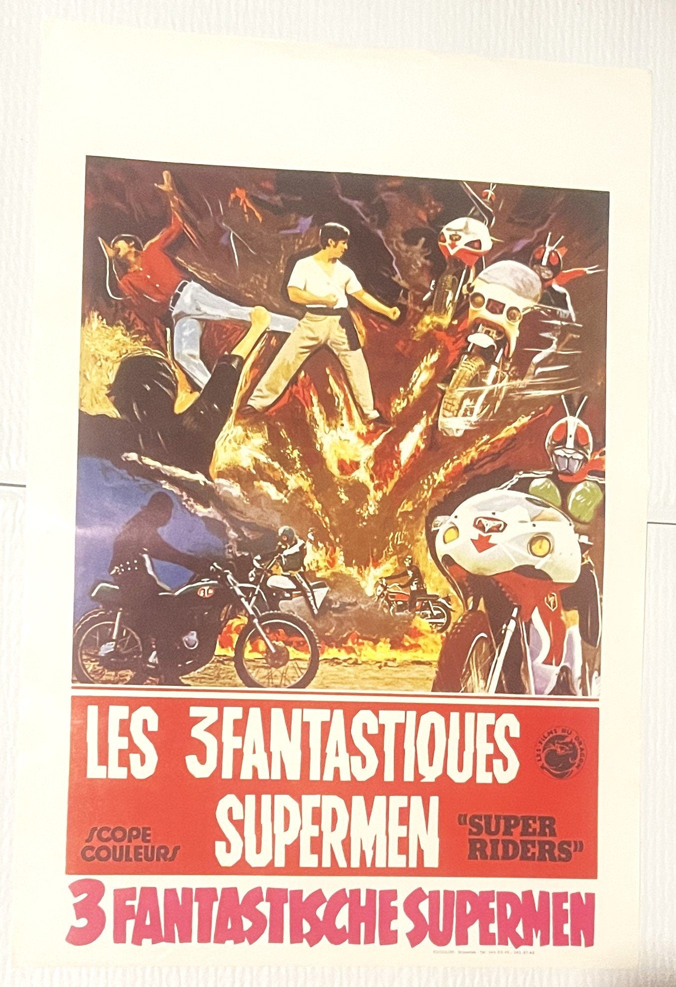 Vintage Belgian movie poster showing three costumed superhero riders on motorcycles amid explosions and flames, with red and 