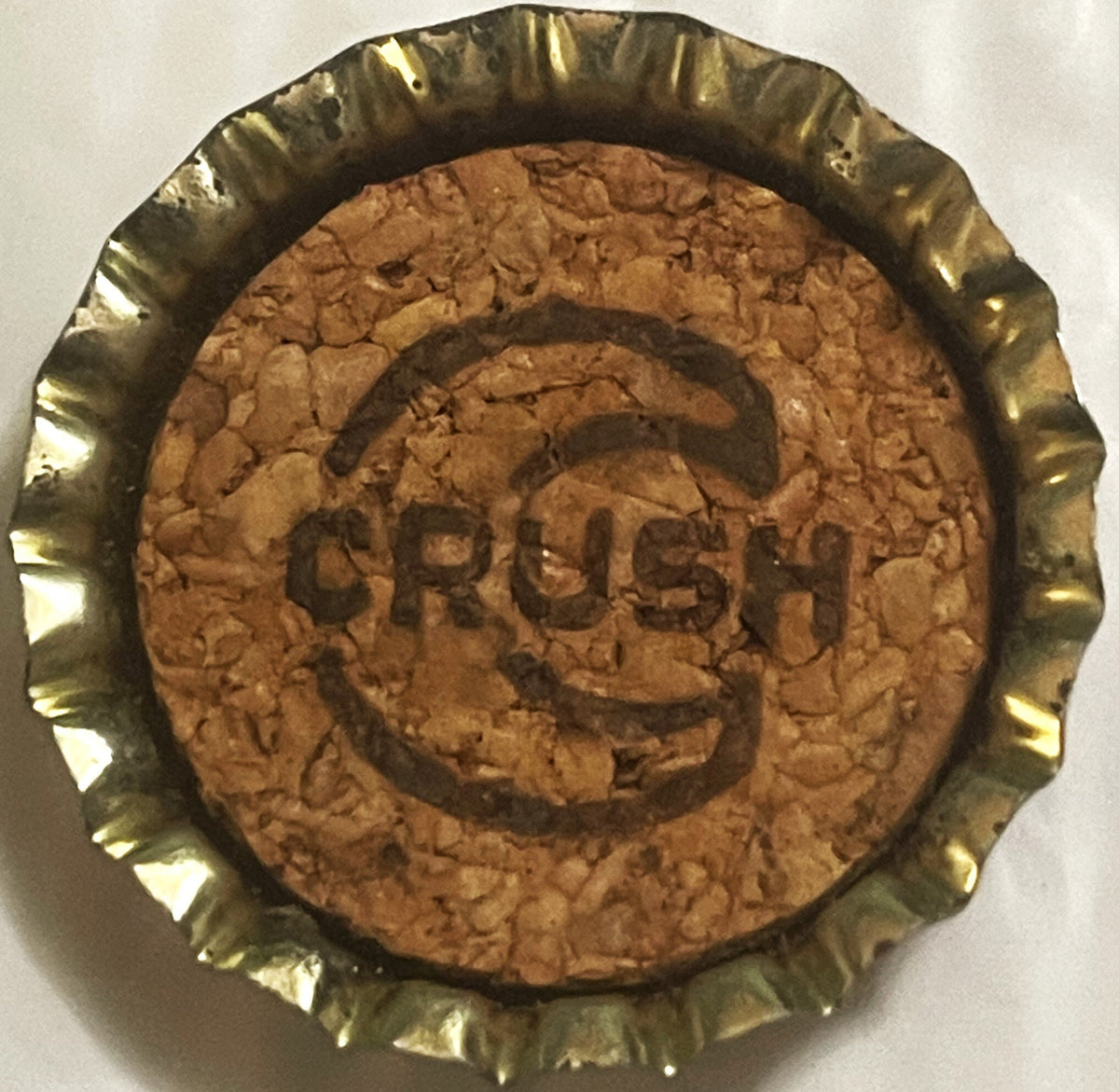 Vintage Strawberry Crush soda bottle cap with cork lining, showing embossed text on brown cork surface in gold metal rim, vie