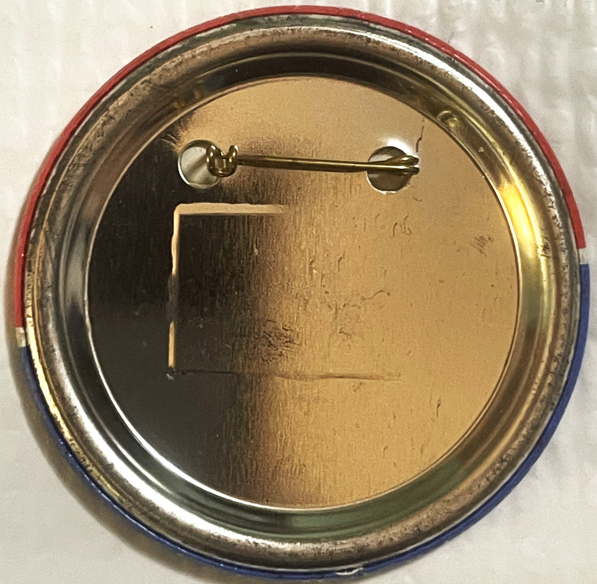 The reverse of the large button: a plain brass-toned back inside the rolled red, white and blue rim, with the pin across the top.