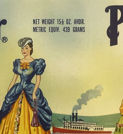Vintage can label featuring elegant woman in blue and yellow dress with steamboat on river, net weight 15½ oz marked at top